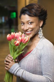 Attractive young African-American woman smiles for the camera. She is holding a bouquet of tulips. Vertical shot.