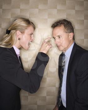 Caucasian mid-adult businesswoman yelling and pointing at middle-aged businessman. Vertical format.
