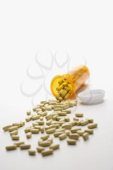Yellow pill bottle with brown tablets spilling out onto a white surface. Vertical shot. Isolated on white.
