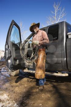 Man standing with a lariat next to the open door of a pickup truck. Vertical shot.