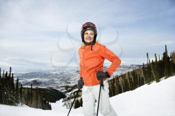 Smiling skier on ski slope in Colorado leaning on her poles with mountains in background. Horizontal shot.