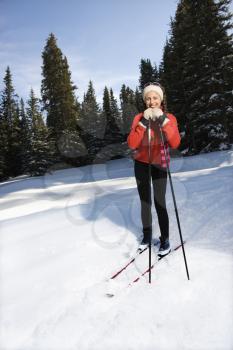 Female snow skiier smiling, standing in the snow leaning on ski poles.  Vertically framed shot.