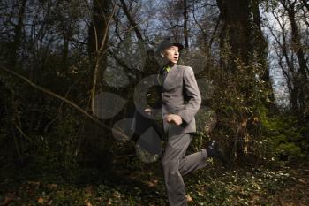 Young businessman runs through the woods, looking behind him while holding a briefcase. Horizontal shot.