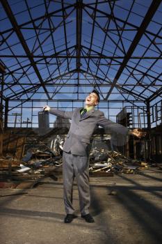 Young businessman smiles with open arms as he stands holding his briefcase in an abandoned building. Vertical shot
