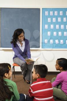 Teacher reading book to young students in classroom. Vertically framed shot.