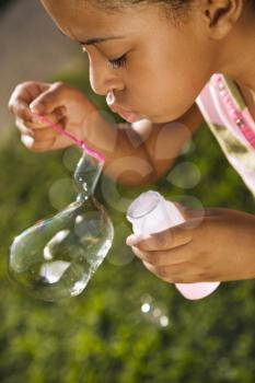 Young girl blowing bubbles outside. Vertically framed shot.