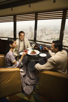 High angle view of young adult males and a female seated near a window in a high rise restaurant. Vertical shot.