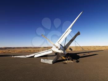 A small, crashed aircraft in a desert landscape. It is on its side with a broken wing and tail. Horizontal shot.