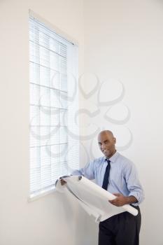 African American businessman reading architectural plans and smiling.