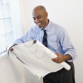 African American businessman reading architectural plans and smiling.