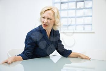 Caucasian middle aged businesswoman grabbing edge of desk looking angry.