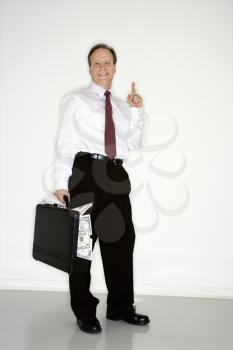 Caucasian middle aged businessman carrying briefcase overflowing with money holding up one finger.