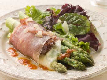 Royalty Free Photo of Roasted Asparagus Spears with Mozzarella Cheese and Sun Dried Tomatoes Wrapped In Prosciutto