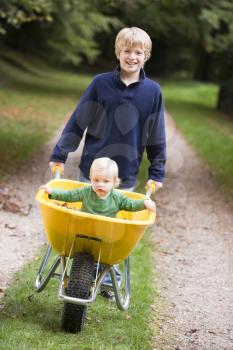 Royalty Free Photo of a Young Boy Pushing a Baby in a Wheelbarrow