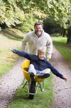 Royalty Free Photo of a Father Pushing a Son in a Wheelbarrow
