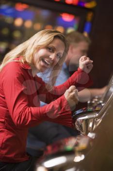 Woman in casino excited playing slot machine with people in background (selective focus)