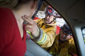 Royalty Free Photo of a Firefighter Taking a Woman's Pulse Behind the Wheel of a Car