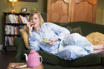 Royalty Free Photo of a Young Woman At Home Eating Cookies and Drinking Tea in the PJs