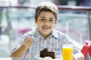 Royalty Free Photo of a Young Boy Eating Cake and Drinking Juice