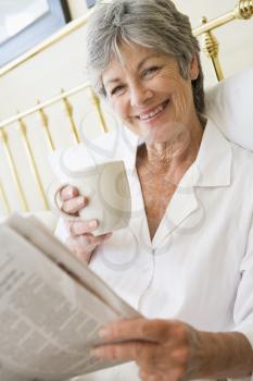Royalty Free Photo of a Woman Reading a Newspaper With a Coffee in Bed