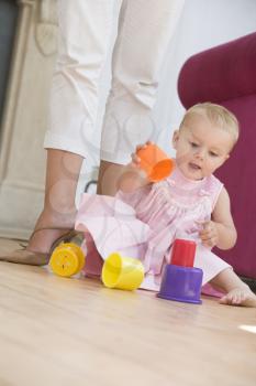 Royalty Free Photo of a Baby Playing on the Floor Beside Her Mother's Legs