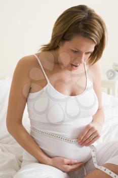 Royalty Free Photo of a Pregnant Woman Measuring Her Stomach and Looking Worried