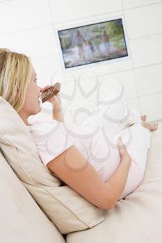 Royalty Free Photo of a Pregnant Woman Eating Chocolate in Front of the TV