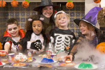 Royalty Free Photo of a Woman in a Witch Hat With Four Young Children Looking at Treats