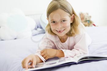 Royalty Free Photo of a Young Girl Lying on a Bed Reading Her Book