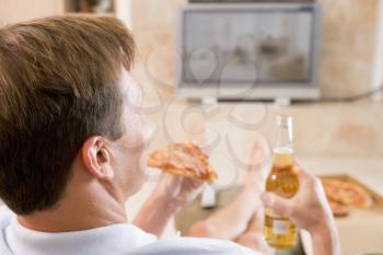 Royalty Free Photo of a Man Drinking Beer and Eating Pizza in Front of the TV