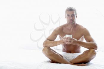 Royalty Free Photo of a Man Sitting on a Bed Drinking Coffee