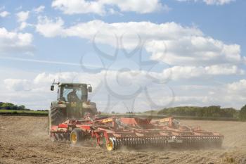 Royalty Free Clipart Image of a Tractor Tilling the Soil