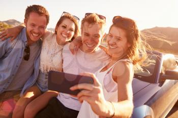Friends On Road Trip Sit On Convertible Car Taking Selfie