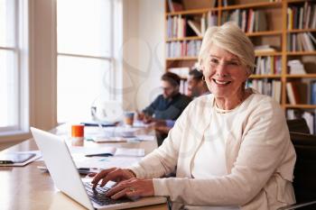 Senior Businesswoman Using Laptop At Desk In Busy Office