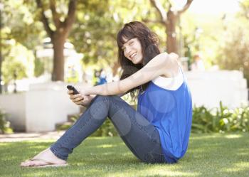 Portrait Of  Teenage Girl Sitting In Park Using Mobile Phone