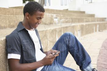 Male Teenage Student Sitting Outside On College Steps Using Mobile Phone