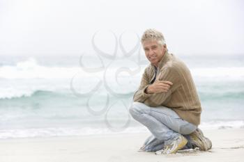 Senior Man On Holiday Kneeling On Winter Beach