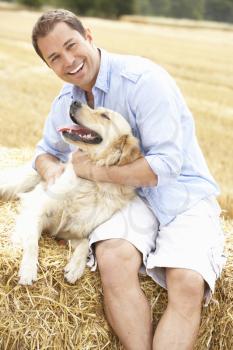 Man Sitting With Dog On Straw Bales In Harvested Field
