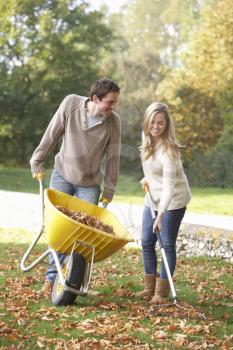 Young couple raking autumn leaves in garden