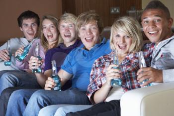 Group Of Teenage Friends Sitting On Sofa At Home Watching Drinking Alcohol