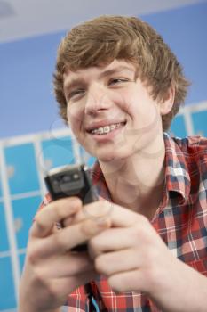 Male Teenage Student Using Mobile Phone By Lockers In School