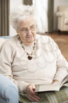 Senior Woman Relaxing In Chair At Home Reading Book