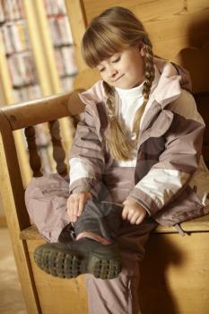 Young Girl Sitting On Wooden Seat Putting On Warm Outdoor Clothes And Boots