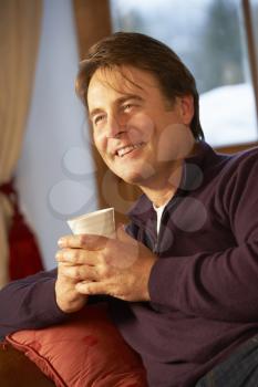 Middle Aged Man Relaxing With Hot Drink On Sofa Watching TV