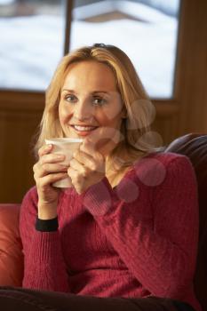 Middle Aged Woman Relaxing With Hot Drink On Sofa Watching TV