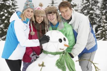 Teenage Family Building Snowman On Ski Holiday In Mountains