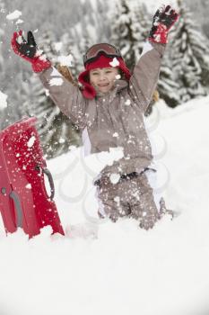 Young Girl Playing In Snow With Sledge On Ski Holiday In Mountains