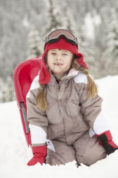 Young Girl Playing In Snow With Sledge On Ski Holiday In Mountains