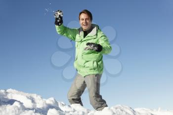 Man About To Throw Snowball Wearing Warm Clothes On Ski Holiday In Mountains