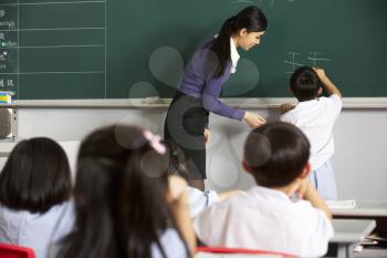 Male Pupil Writing On Blackboard In Chinese School Classroom